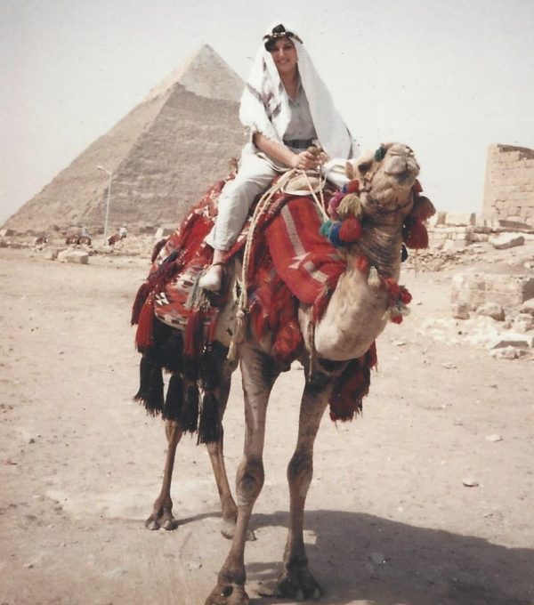 The author sits on a camel, wearing a traditional headdress, in front of the Pyramids at Giza, in Egypt.